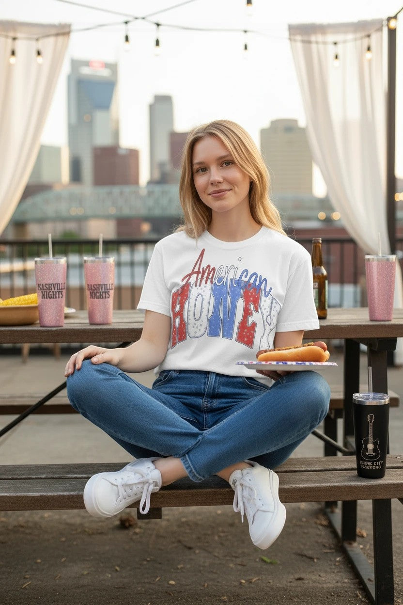 Southern Charm Design Works white cotton t-shirt with "American Honey" graphic in distressed red, white, and blue.