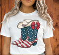 Southern Charm Design Works white t-shirt with patriotic cowboy boots and hat graphic. Boots feature American flag stars and stripes.