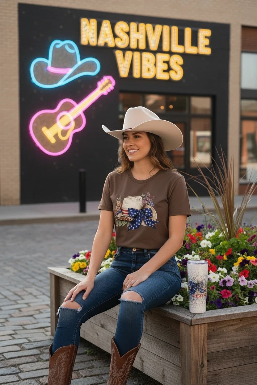 Southern Charm Design Works brown cotton t-shirt with patriotic floral cowboy hat graphic. Model wears ripped jeans and cowboy boots.